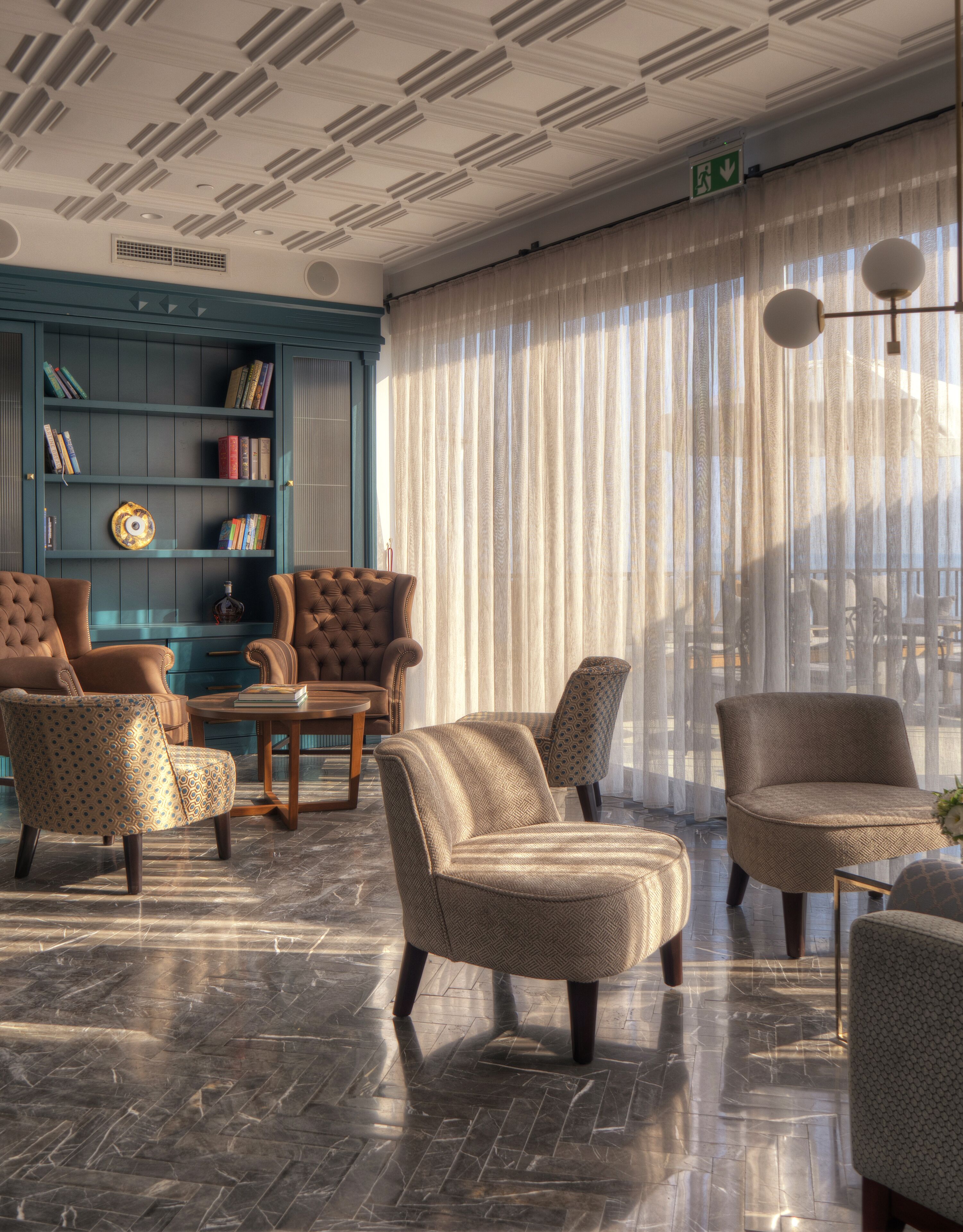 Un salon bien éclairé, doté d’un sol en marbre, d’une bibliothèque bleue et de plusieurs fauteuils rembourrés.