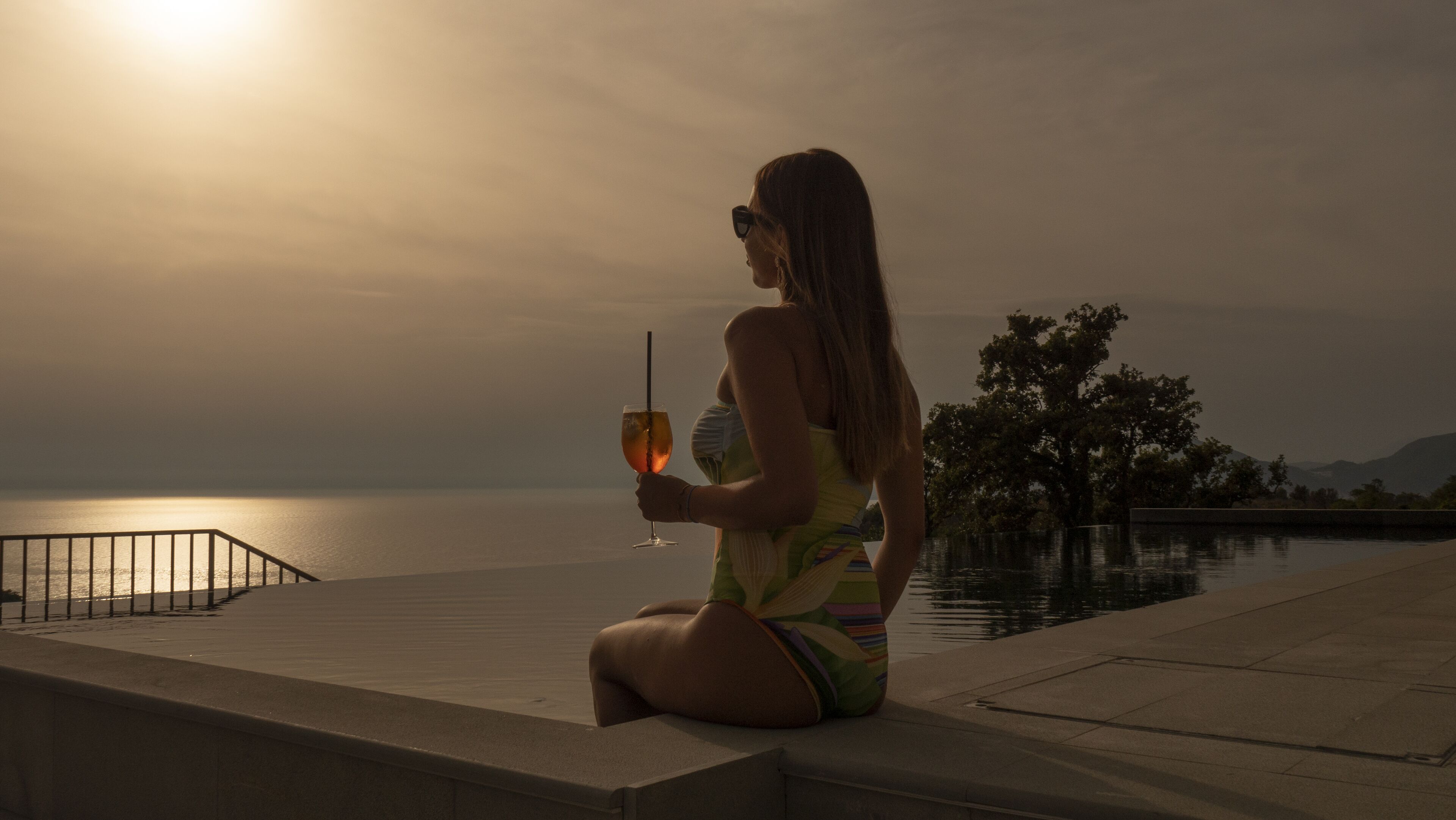 A person sitting on a concrete ledge by a body of water during sunset.