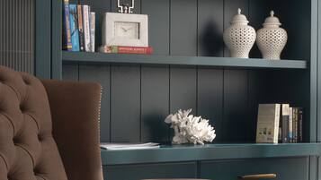 Een donkerblauwe boekenkast met decoratieve koraalstukken, een klok en verschillende boeken.