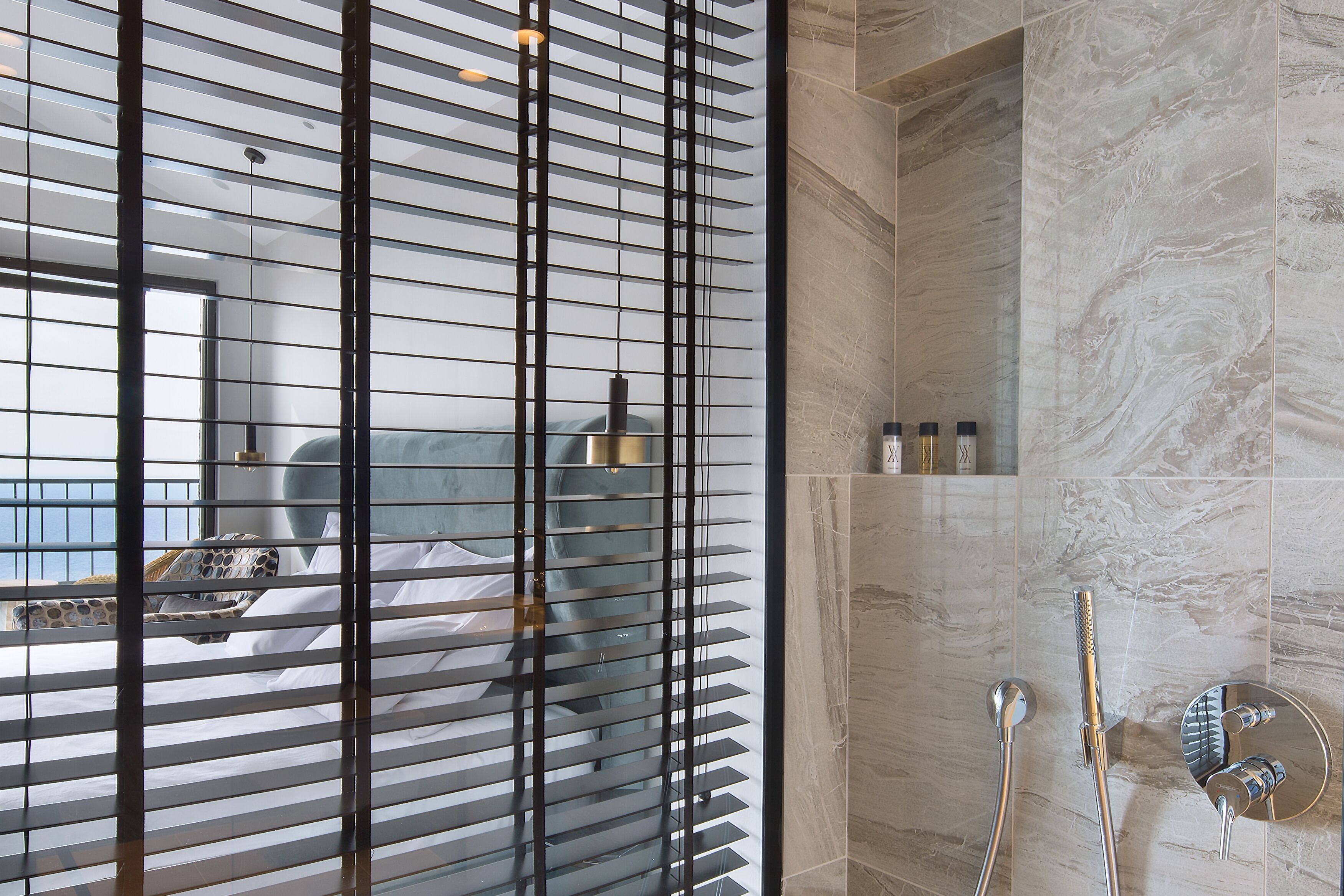 A modern bathroom with a shower, a glass partition, and a view of a bed with a circular headboard.