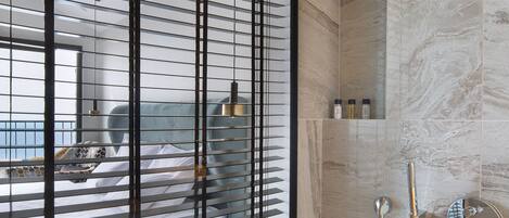 A modern bathroom with a shower, a glass partition, and a view of a bed with a circular headboard.