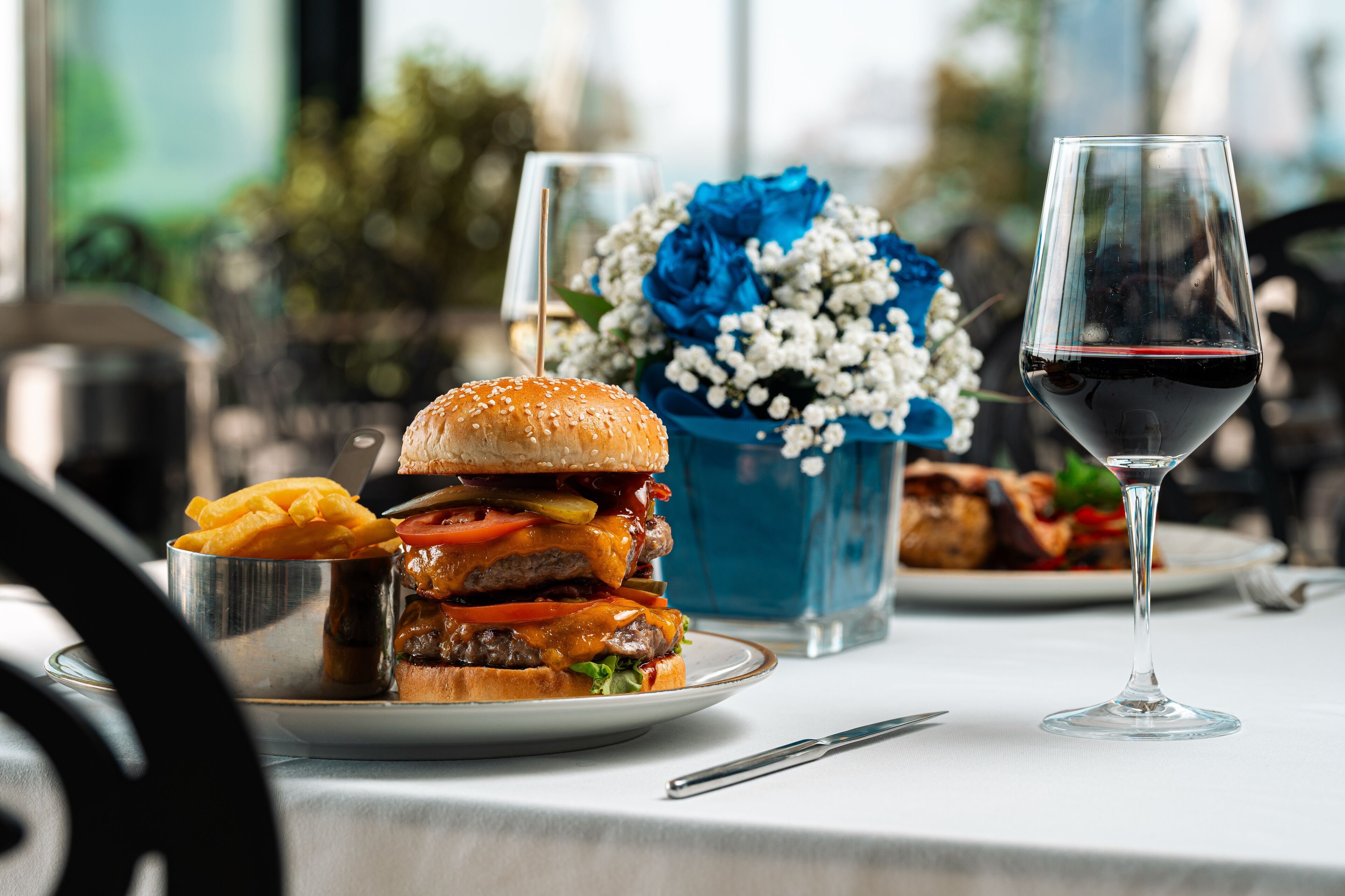 A meal with a burger, fries, and a glass of red wine on a table.