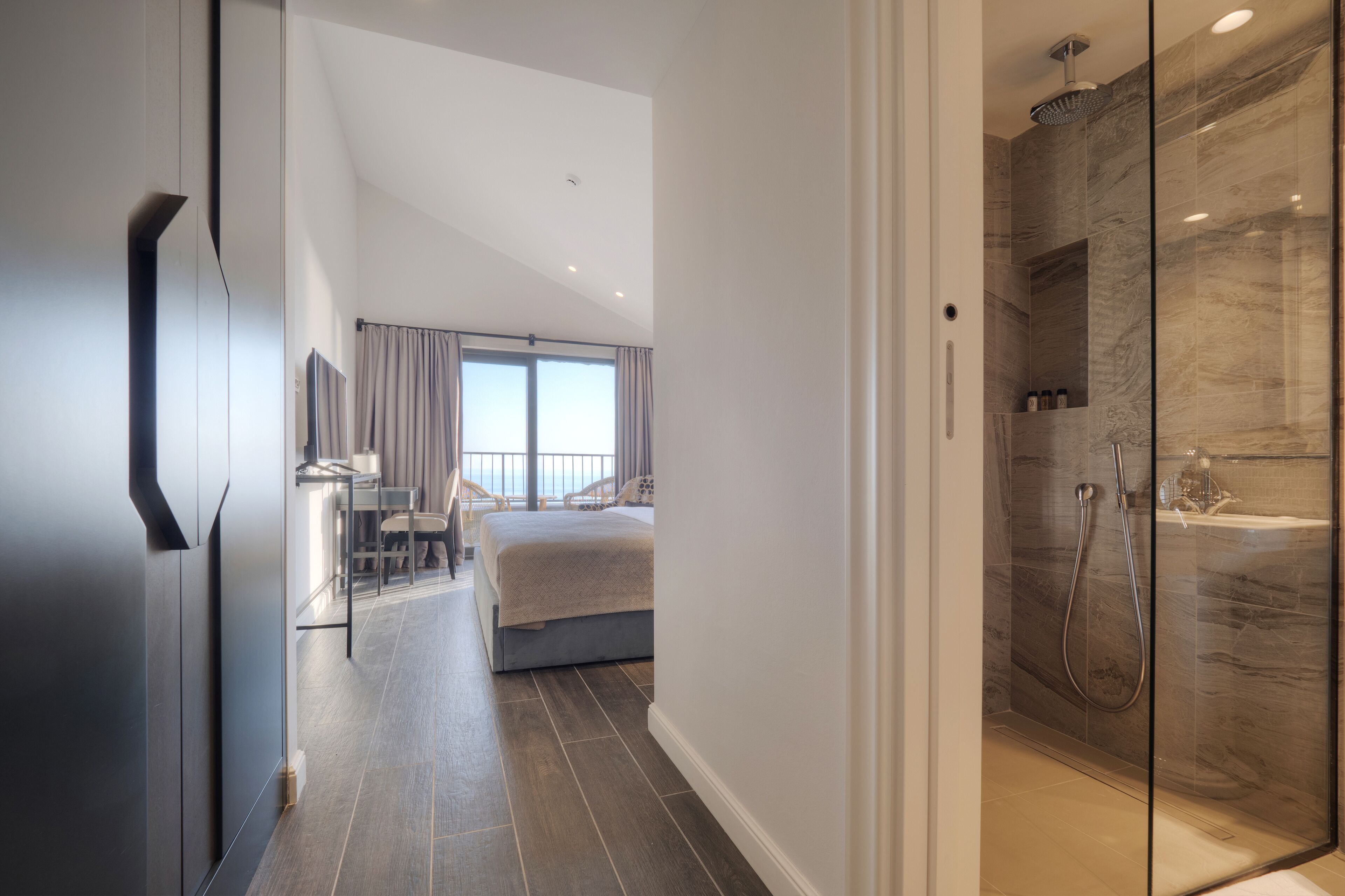 A modern hotel room with a large bed, a desk, and a shower area.