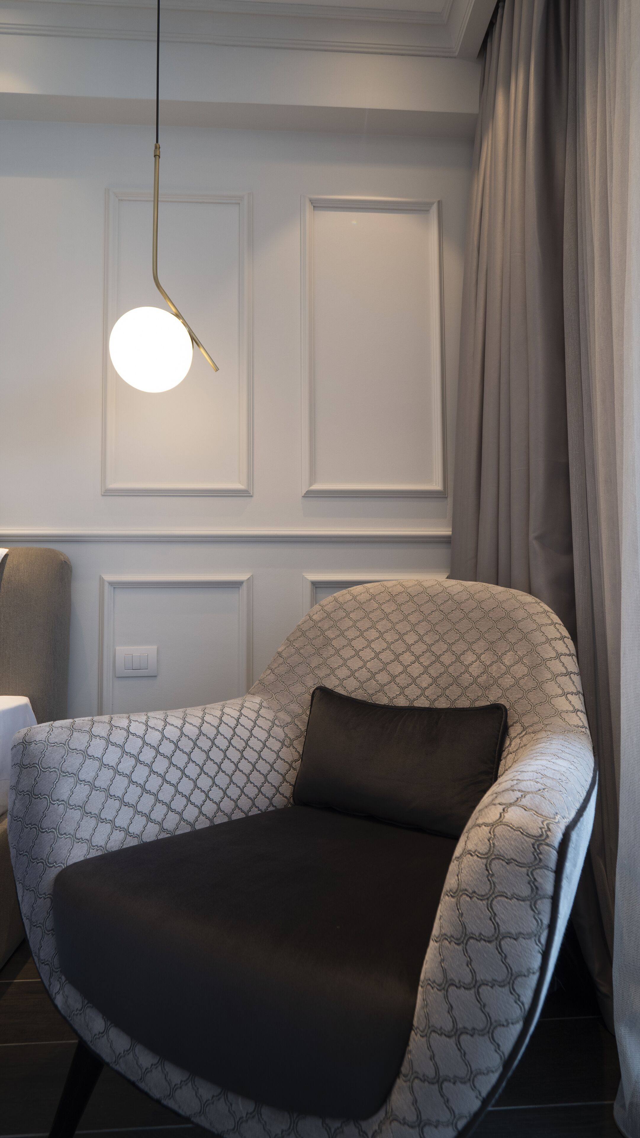 A modern armchair with a geometric pattern, a round pendant light, and a white wall with paneling.