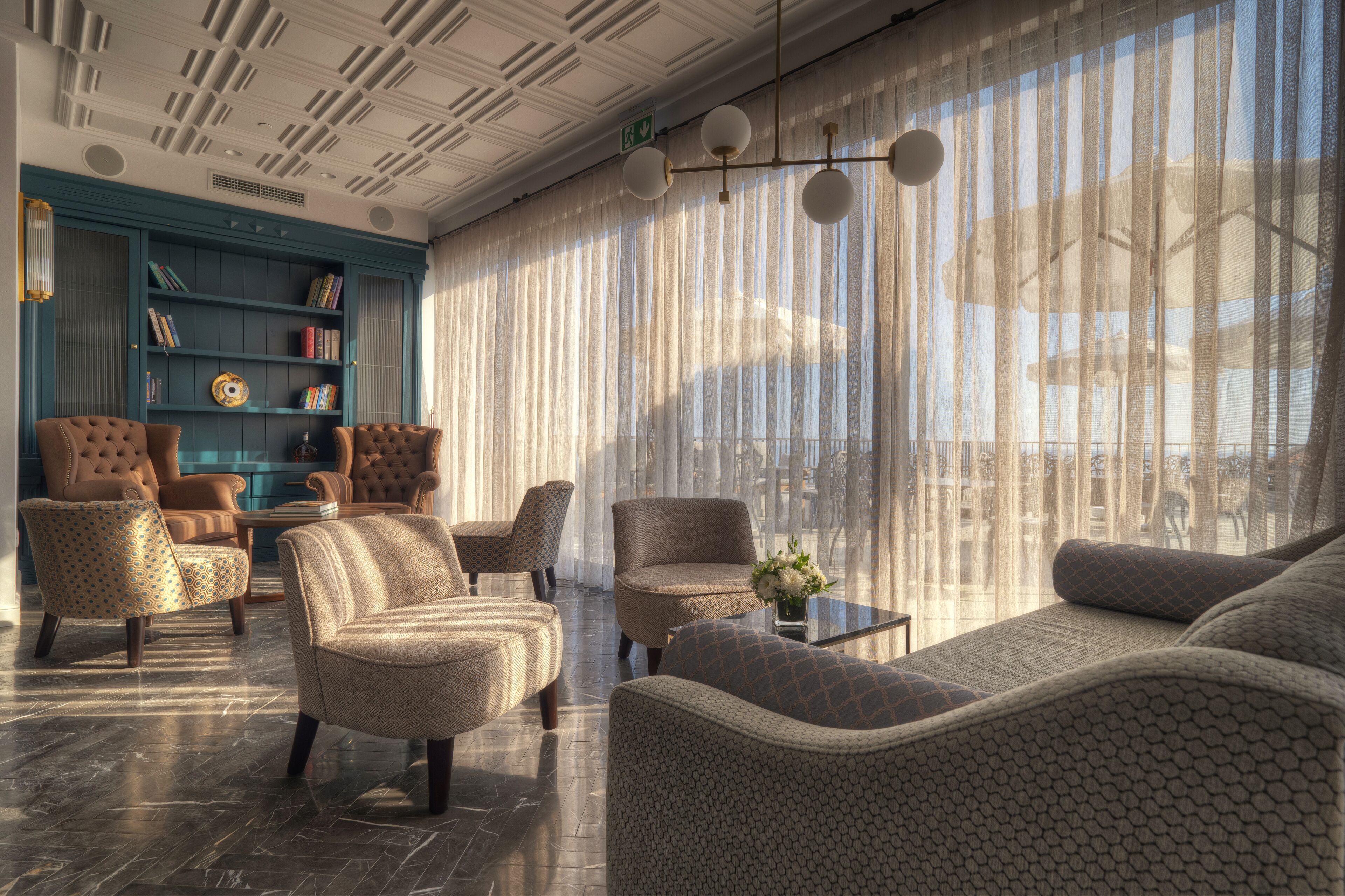 A modern lounge with a large window, comfortable seating, and a bookshelf.