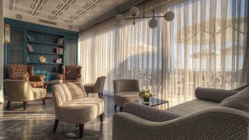 A modern lounge with a large window, comfortable seating, and a bookshelf.
