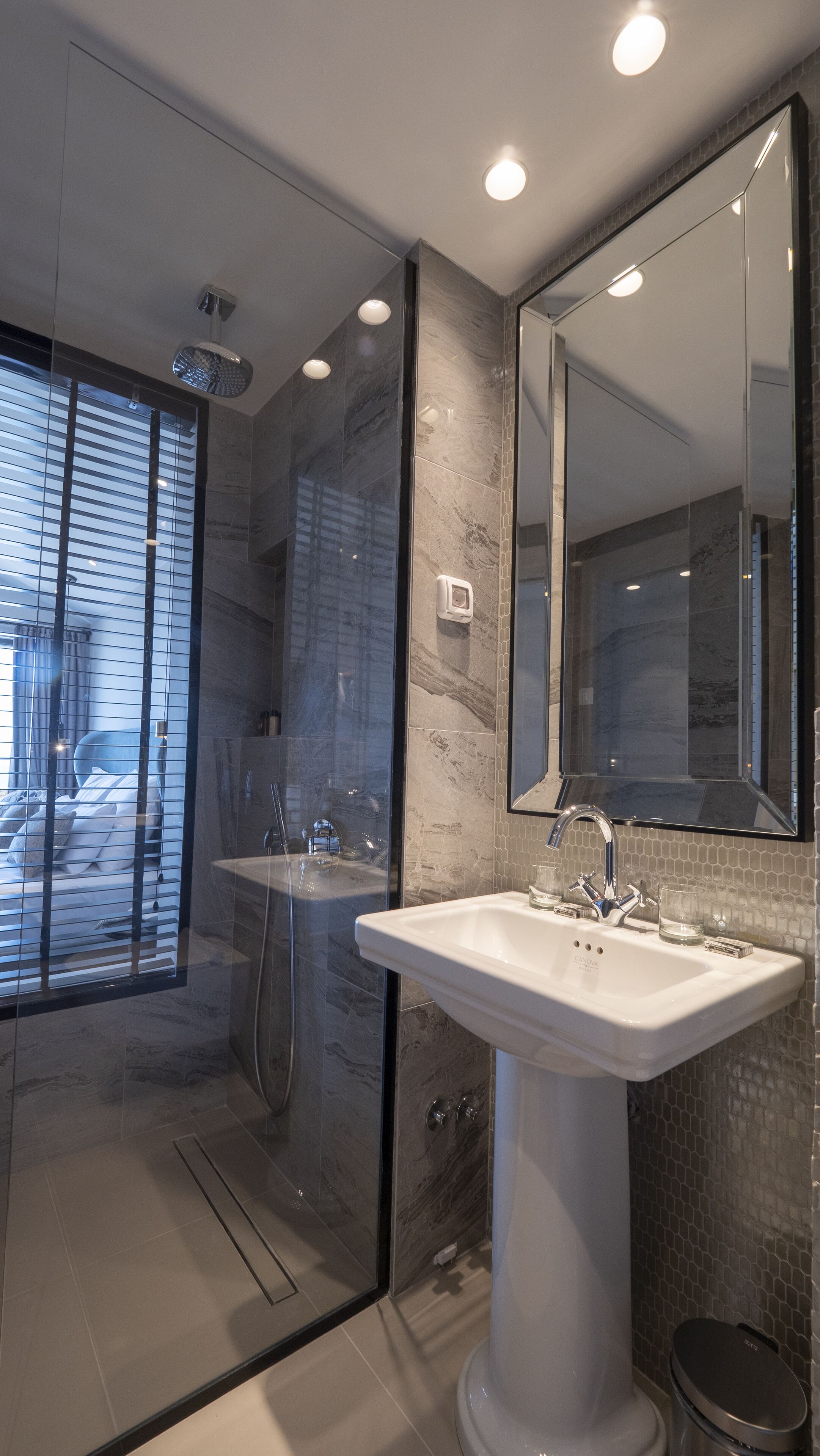 A modern bathroom with a glass shower enclosure, a pedestal sink, and a large mirror.
