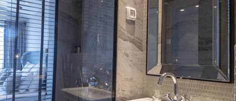 A modern bathroom with a glass shower enclosure, a pedestal sink, and a large mirror.