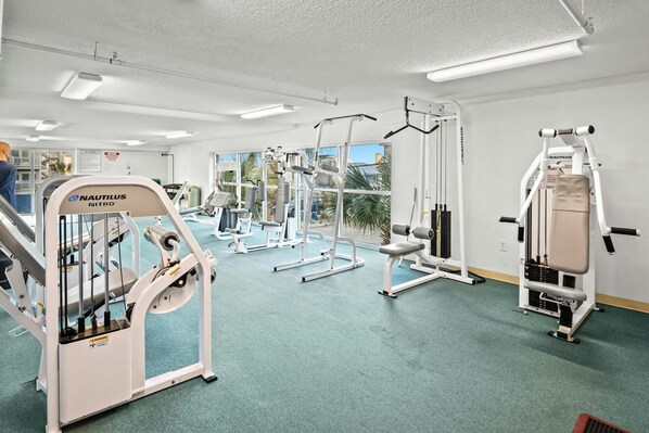 A gym with Nautilus equipment, large windows, and a green carpet.
