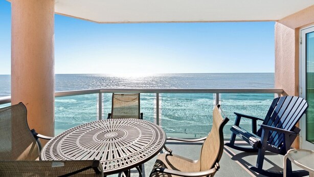 Een balkon met een ronde tafel en twee stoelen, met uitzicht op de oceaan.
