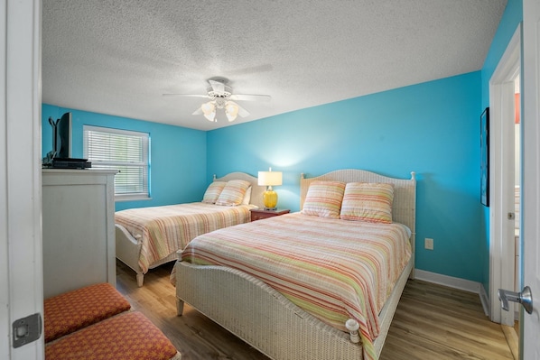 A bedroom with two beds, a ceiling fan, a nightstand with a lamp, and a window with blinds. - Spacious three bedroom in Cherry Grove | Laguna Keyes - 1109 (North Myrtle Beach)