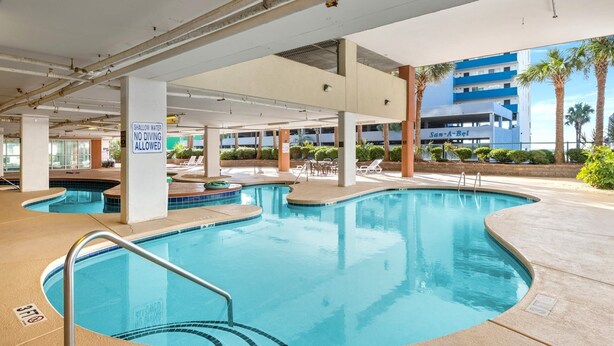 A pool area with multiple pools, a sign indicating shallow water no diving allowed, and a building labeled "San-A-Bel" in the background.