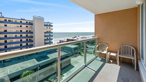A balcony with a view of the beach and a parking area.