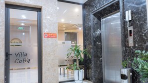 An elevator, a potted plant, and a door with a sign reading "Villa Coffee". - Hotel Villa Ju (Hanoi)
