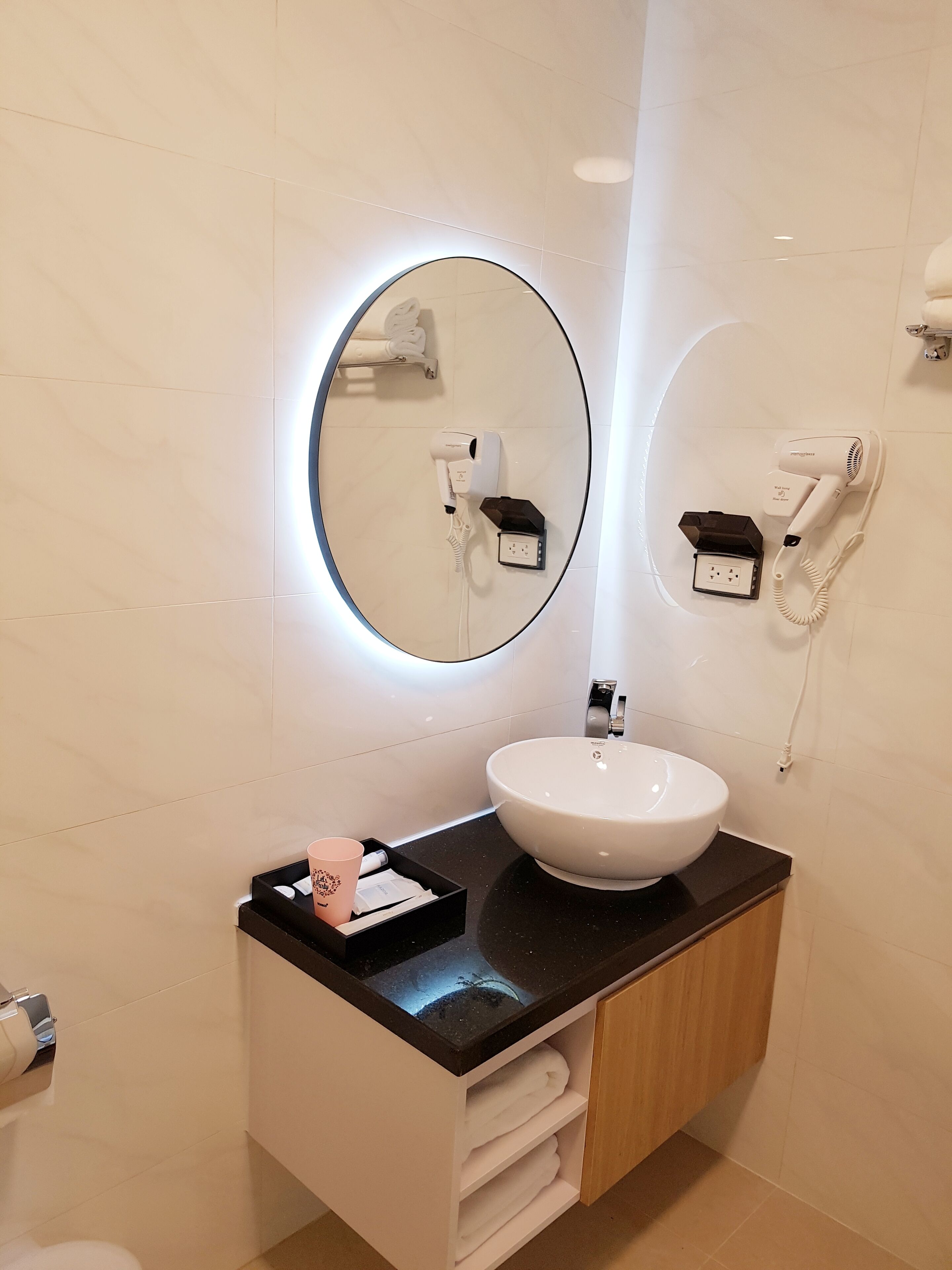 Ein modernes Badezimmer mit einem runden Spiegel, einem Waschbecken und zwei an der Wand befestigten Haartrocknern.