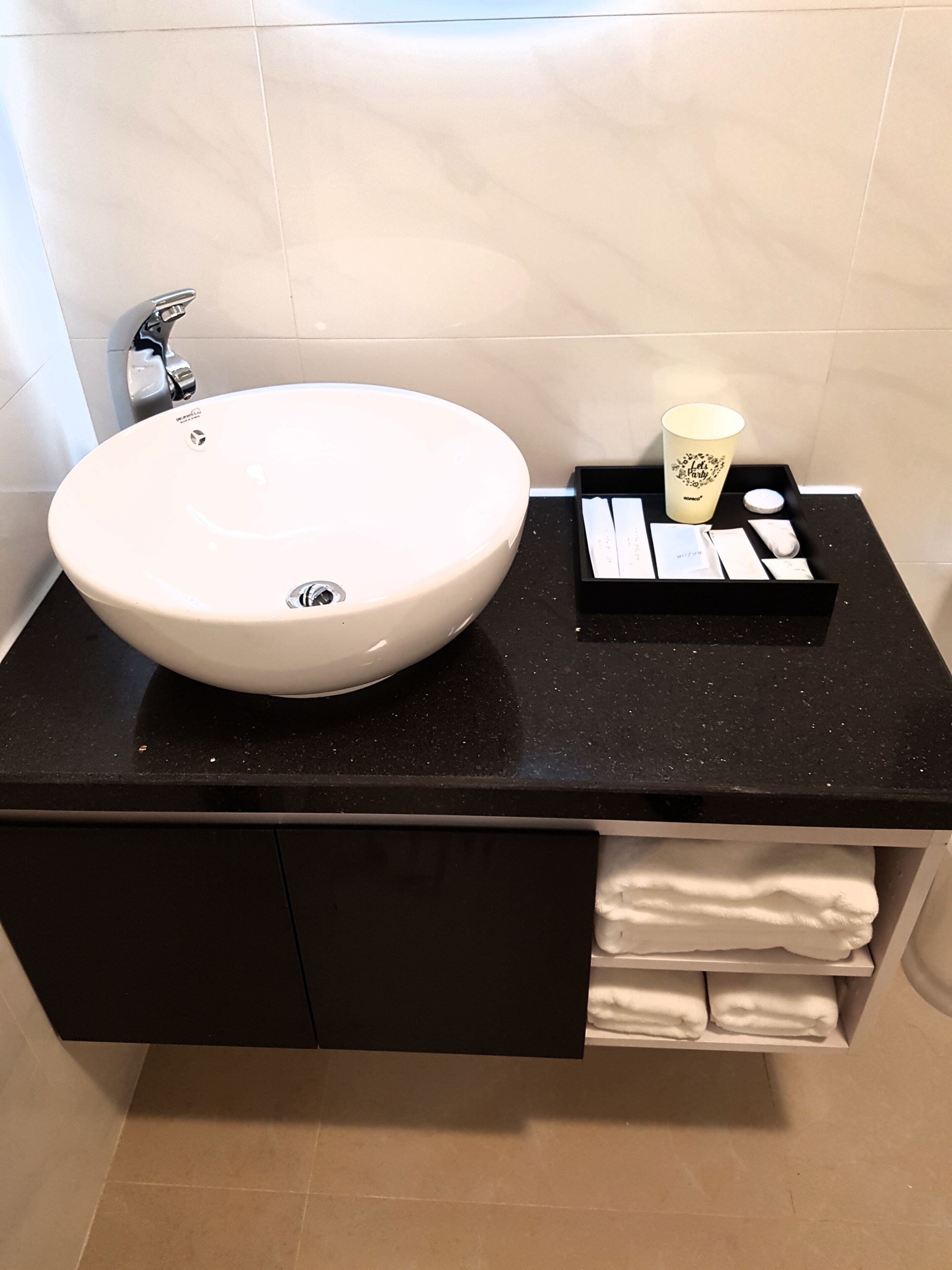 Une salle de bain avec un grand lavabo blanc, un plan de toilette noir et un porte-serviettes où sont pliés des serviettes.