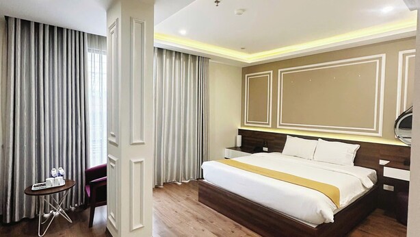 A modern hotel room with a large bed, wooden flooring, a small table with amenities, and a large mirror. - Hotel Villa Ju (Hanoi)