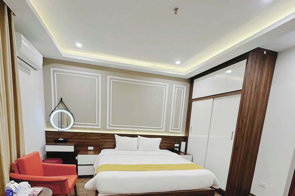 A hotel room with a large bed, a bedside table, a chair, a mirror, and a wardrobe.