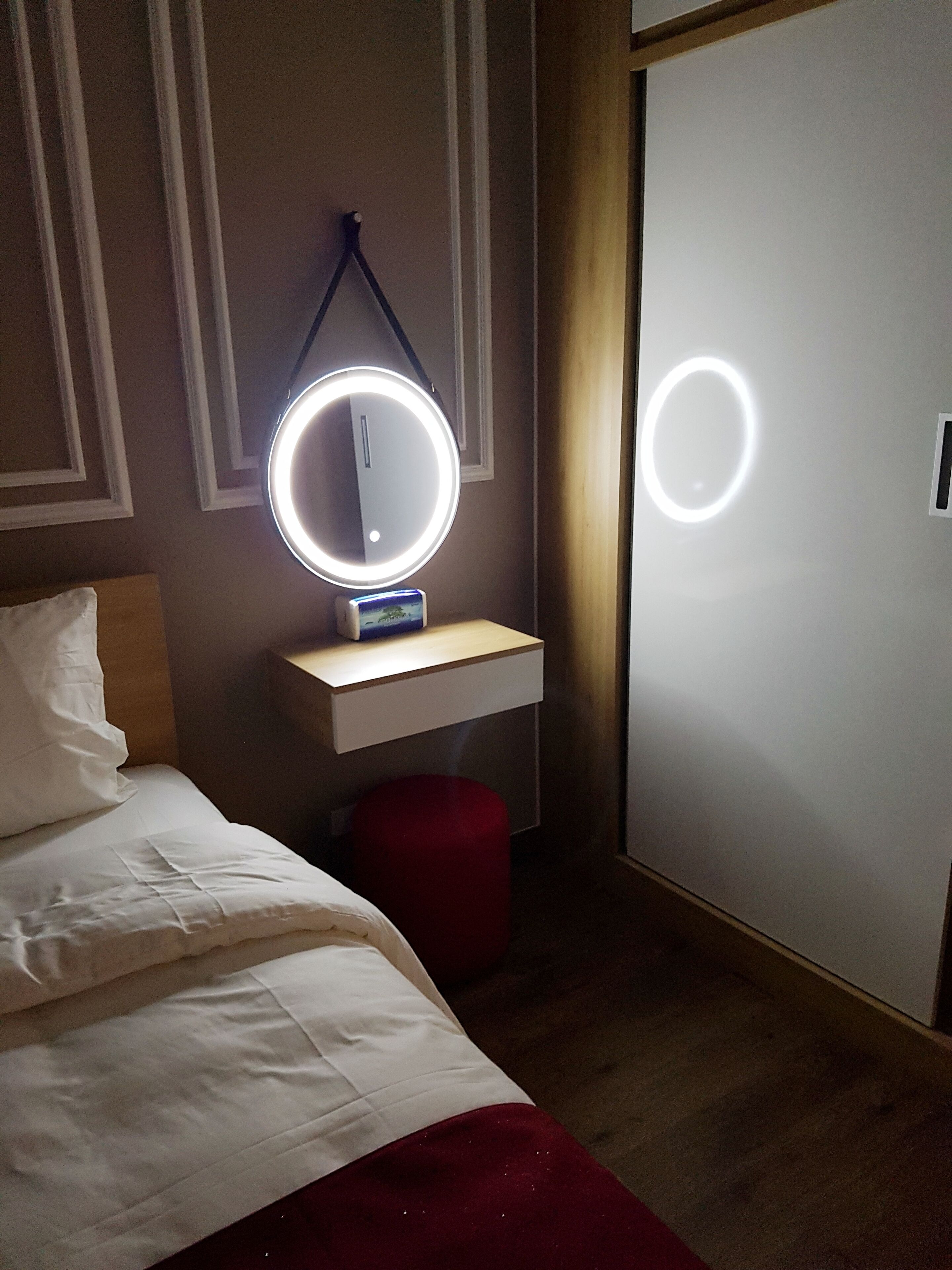 Une chambre d’hôtel avec un lit, une table de chevet surmontée d’un miroir rond et une armoire.