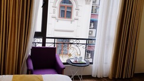 A hotel room with a bed, a purple chair, a small table with a tray, and a view of the outside balcony. - Hotel Villa Ju (Hanoi)