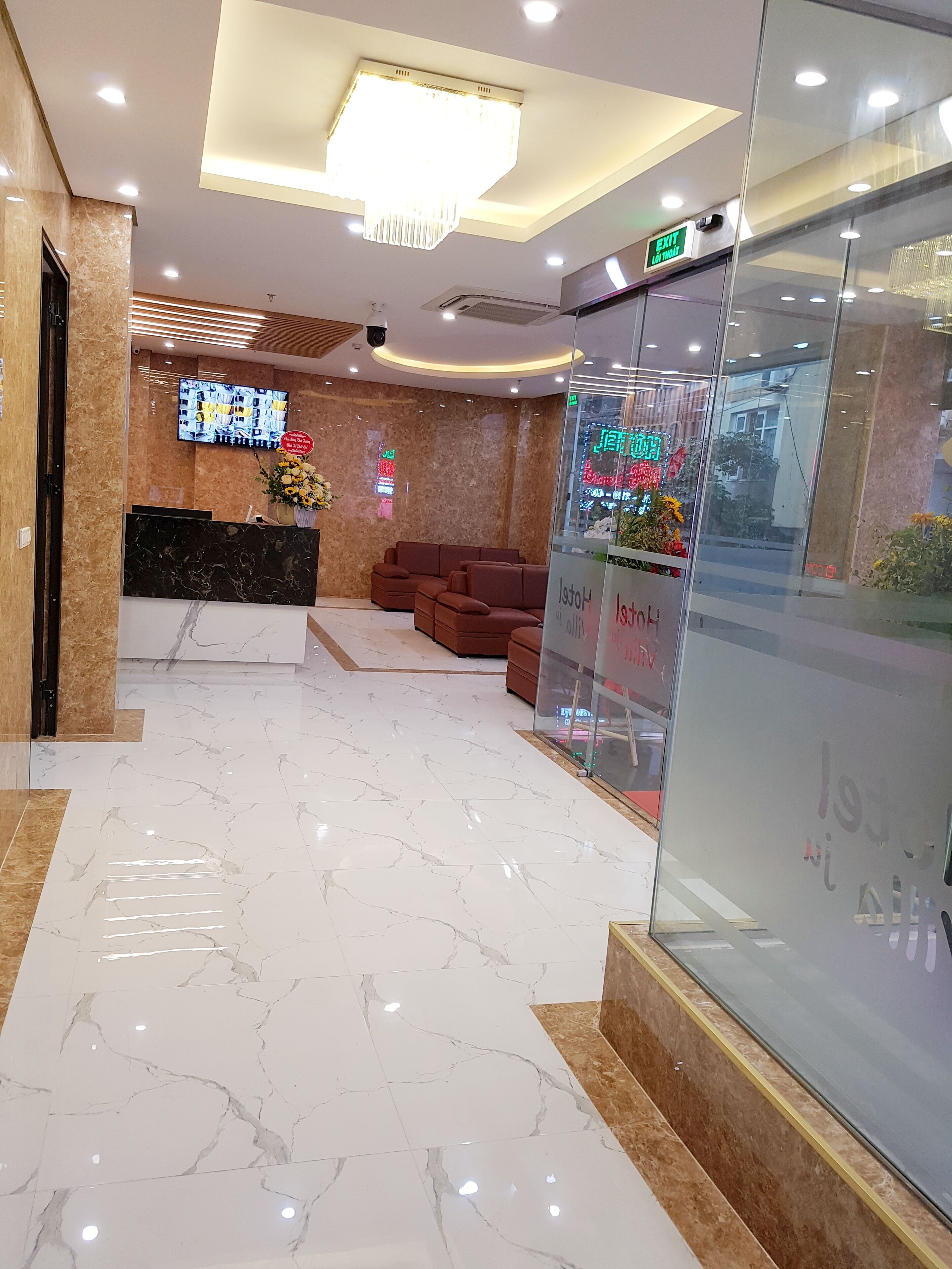 A hotel lobby with a reception desk, seating area, and a glass wall with neon signs.