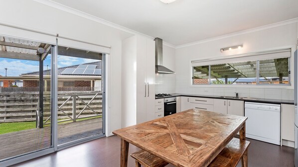 Una cocina moderna con armarios blancos, una mesa de comedor de madera y un ventanal corredizo que da a un patio trasero.