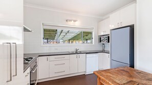 Una cocina moderna con armarios blancos, microondas integrado y un amplio ventanal con vistas a una estructura verde.