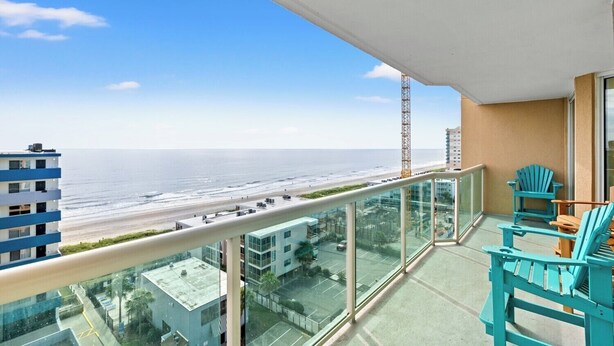 A balcony with a view of the beach and ocean, turquoise chairs, and a glass railing. - 3-bedroom, 8th floor ocean view condo | Malibu Pointe - 805 (North Myrtle Beach)