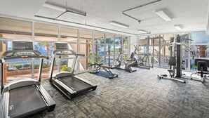 A modern gym with treadmills, elliptical machines, and weight equipment. Large windows offer views of a landscaped area and a body of water. - 3-bedroom, 8th floor ocean view condo | Malibu Pointe - 805 (North Myrtle Beach)