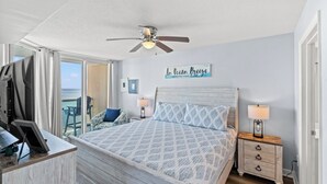 Un dormitorio con cama, mesitas de noche, ventilador de techo y vistas al océano.
