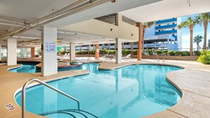 Un área de piscina con varias piscinas, un cartel que indica agua poco profunda, prohibido bucear, y un edificio con el letrero "San-A-Bel" al fondo.
