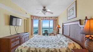 A hotel room with a bed, a TV, a wooden dresser, a lamp, and a view of the ocean. - Perfect 3 bedroom condo, just across from the beach! | Malibu Pointe - 1105 (North Myrtle Beach)