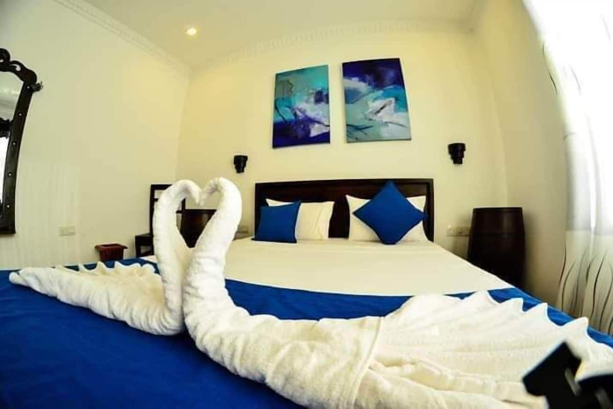 Een hotelkamer met een bed, twee schilderijen aan de muur, een nachtkastje en een lamp.