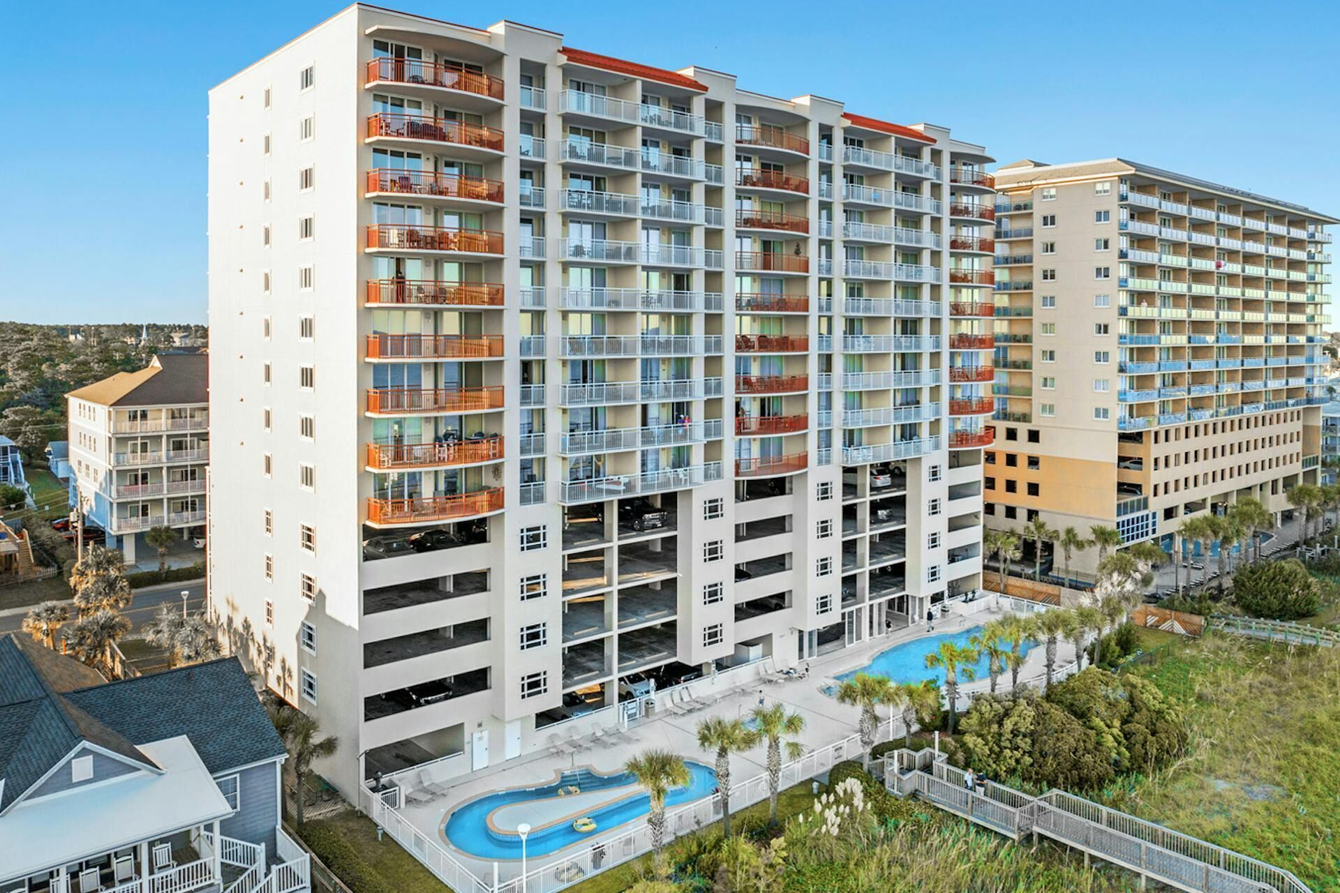 A multi-story hotel with balconies, a swimming pool, and a landscaped area.