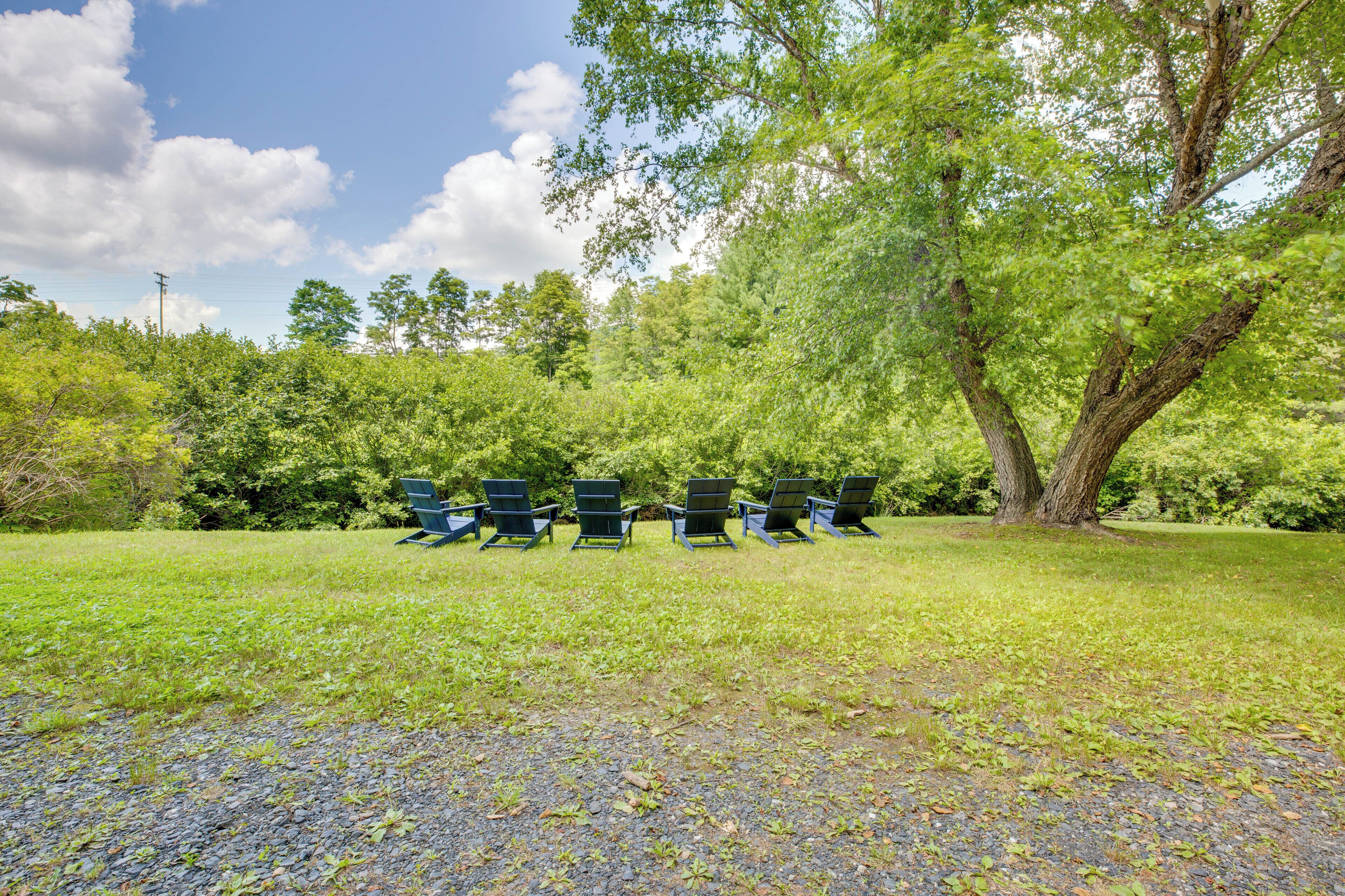 A row of green Adirondack chairs in a grassy area with trees in the background.
