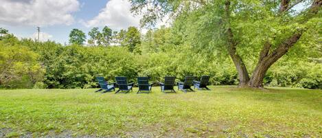 A row of green Adirondack chairs in a grassy area with trees in the background.