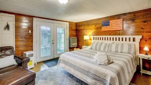 Une pièce avec un lit, un mur en bois, une porte, une fenêtre et un luminaire au plafond.