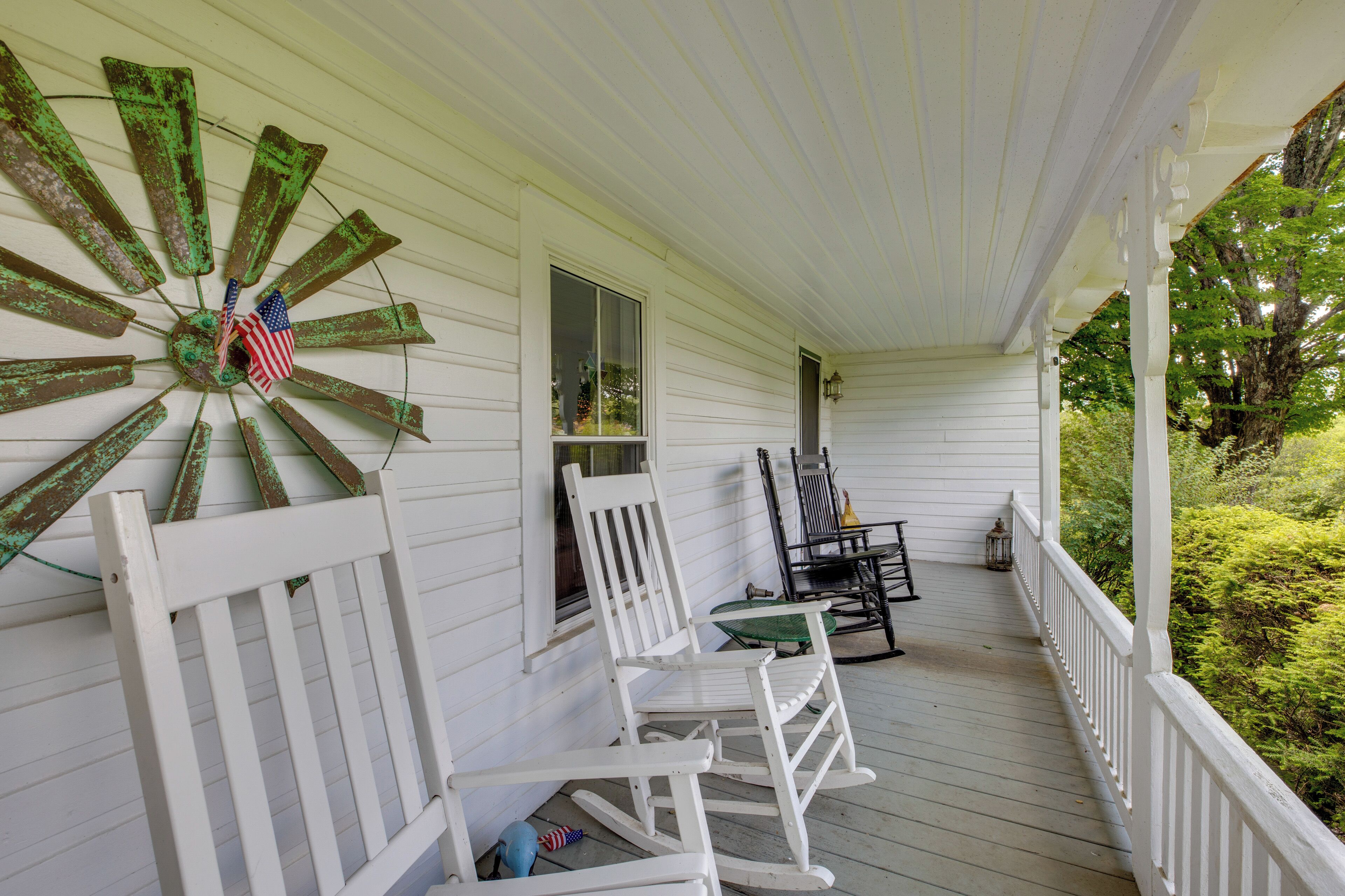 Eine Veranda mit weißen Holzbalkonen, Schaukelstühlen und einem dekorativen Holzwindrad mit einer amerikanischen Flagge.