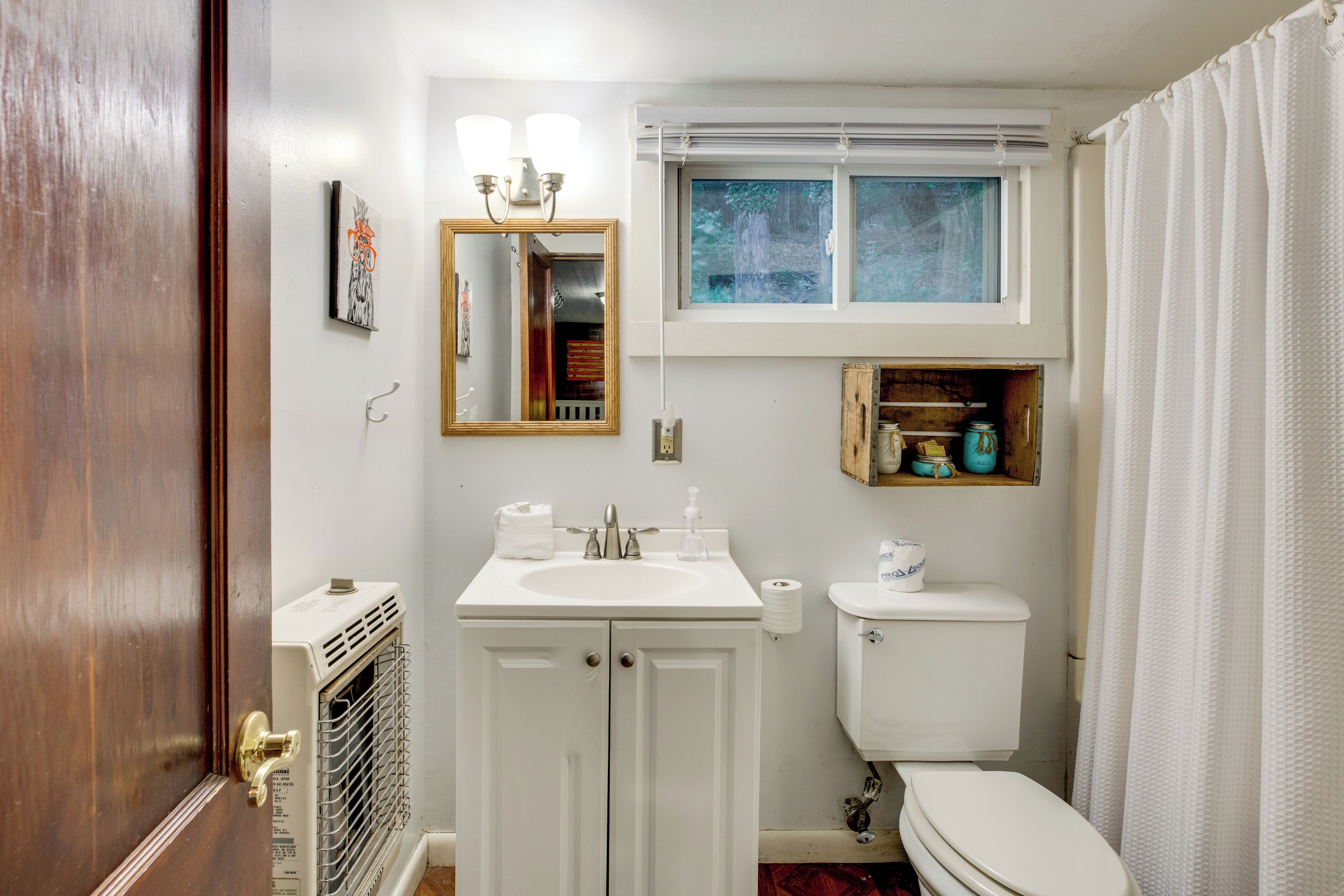 Un baño con lavamanos blanco, espejo, ventana y retrete.