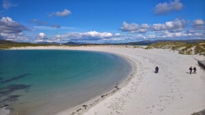 A beach with clear turquoise water, white sand, and a few people walking. - Roundstone Quay (Roundstone)