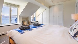 A bedroom with a large bed, a window with a view of the sea, a chair, and a wardrobe. - Roundstone Quay (Roundstone)