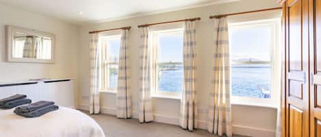 Une chambre d’hôtel avec un lit, une fenêtre avec des rideaux, une vue sur la mer et une armoire en bois.