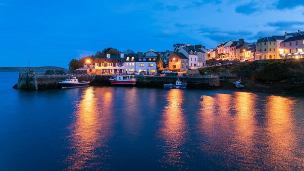 A waterfront town with buildings along the shore, boats docked, and a calm river reflecting the lights. - Roundstone Quay (Roundstone)