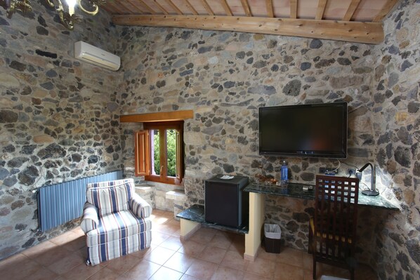 Una habitación con paredes de piedra, un televisor, una mesita, una silla y un radiador.
