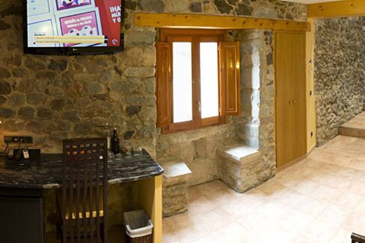 Ein Schlafzimmer mit Steinwand, einem Bett, einem Holz-Kopfteil, einem Fenster, einer Steinsitzbank und einem Steinkamin.