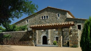 Un edificio de piedra con techo de tejas, entrada con reja y un pequeño porche.