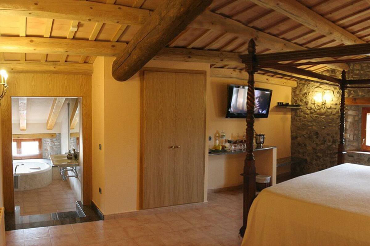 Ein Schlafzimmer mit Himmelbett, Steinwand, Fernseher über einem Waschbecken und Holzboden.