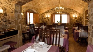 Comedor de paredes de piedra con mesas dispuestas para una comida, destacando un techo alto en arco y sillas de madera.