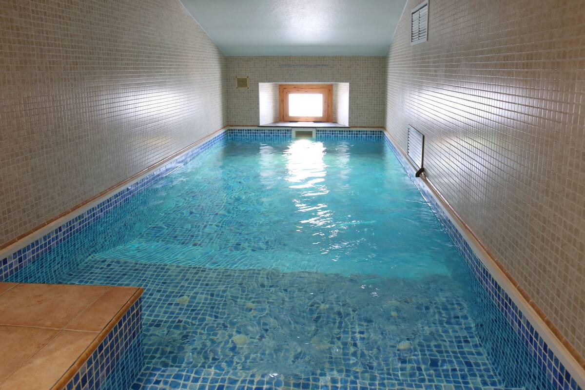 Ein Hallenbad mit klarem, blauen Wasser, gefliesten Wänden und einem Fenster am hinteren Ende.