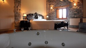 Un dormitorio con pared de piedra, una cama grande, una bañera y dos lámparas fijadas a la pared.